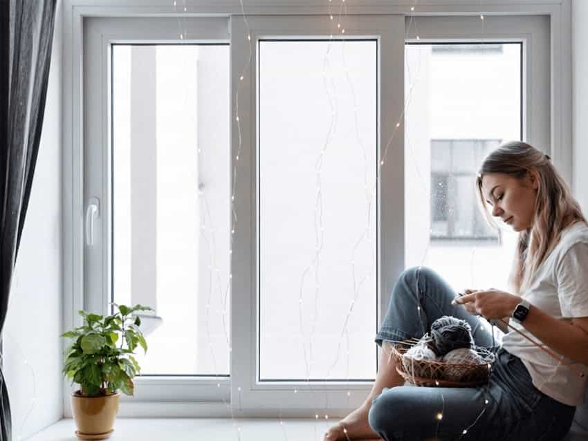 uPVC Double Glazed Windows Options Woman sitting by a three-panel white uPVC sliding window with fairy lights